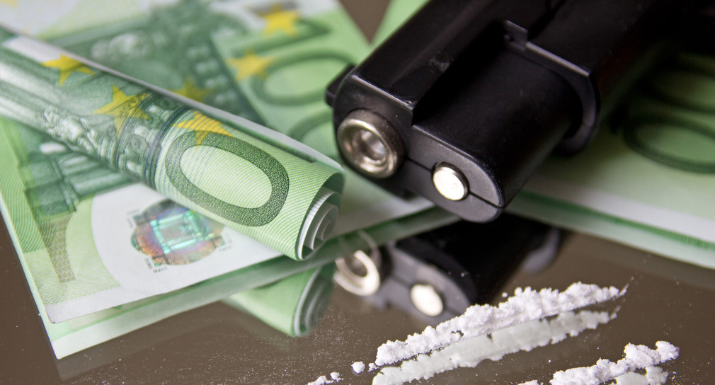 Geldscheine, Pistolenlauf und Drogen.