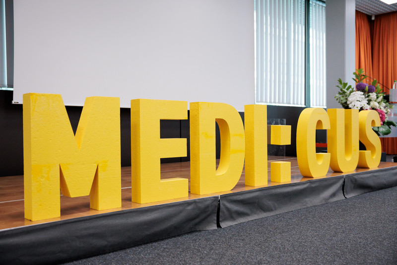 Schriftzug „MEDI:CUS“ auf einer Bühne