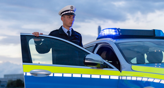 Junger Polizeibeamter vor einem Streifenwagen.