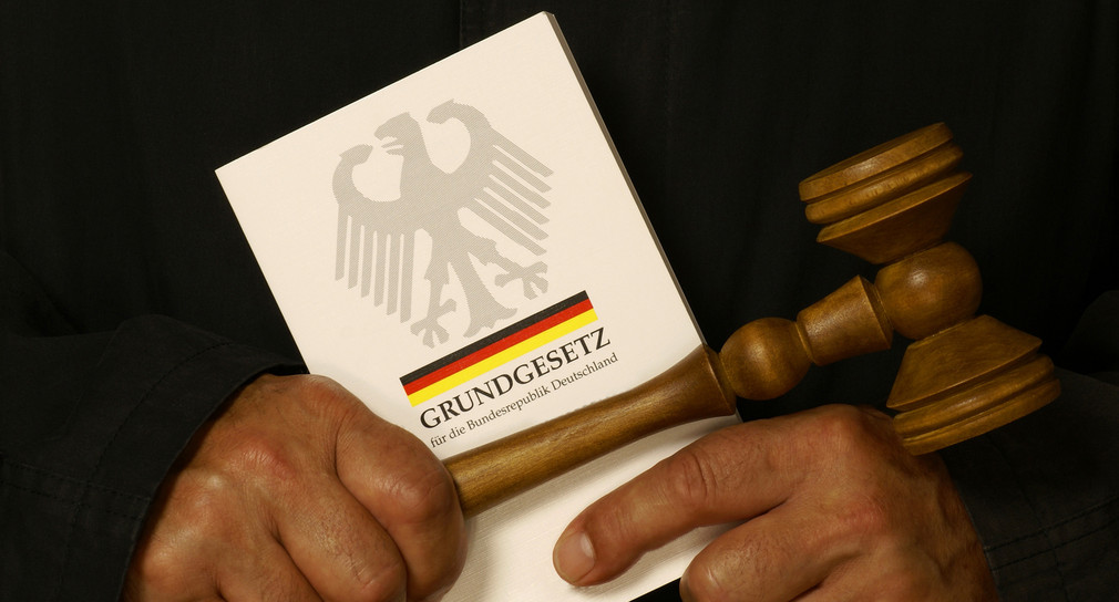 Richter mit Grundgesetz und Richterhammer in den Händen. Quelle: Fotolia.