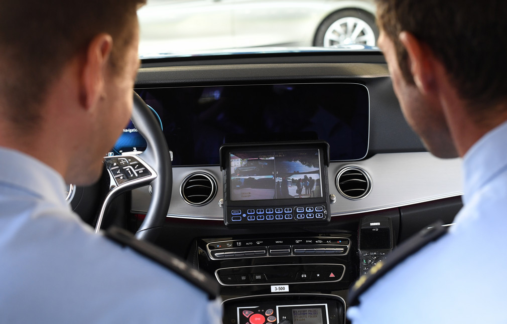 Zwei Polizeibeamte sitzen im Polizeiauto und schauen auf einen Bildschirm, der Aufnahmen des neuen Dashcam-Systems zeigt.
