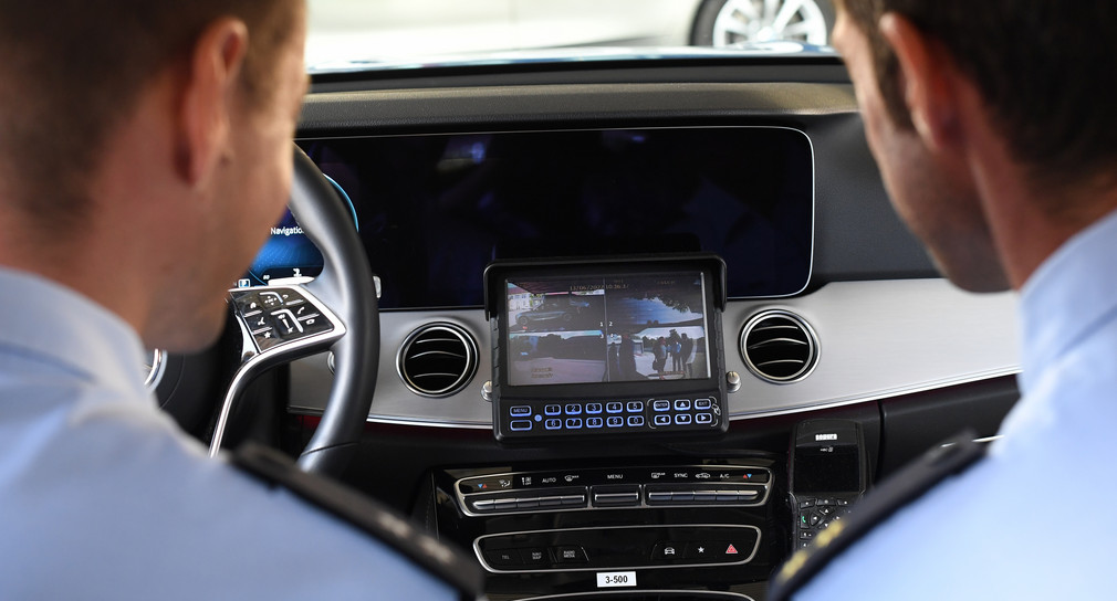 Zwei Polizeibeamte sitzen im Polizeiauto und schauen auf einen Bildschirm, der Aufnahmen des neuen Dashcam-Systems zeigt.