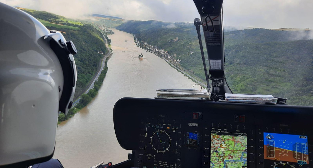 Blick aus dem Cockpit eines Hubschraubers auf einen überschwemmten Fluss.