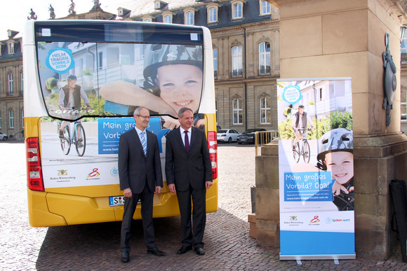Stefan Bender, Vorstandsmitglied der PSD Bank, und Innenminister Reinhold Gall vor einem Bus mit der Beklebung der Radhelmkampagne „Helm tragen. Vorbild sein!“