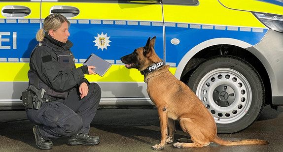 Polizistin mit Datenträgerspürhund vor Dienstwagen