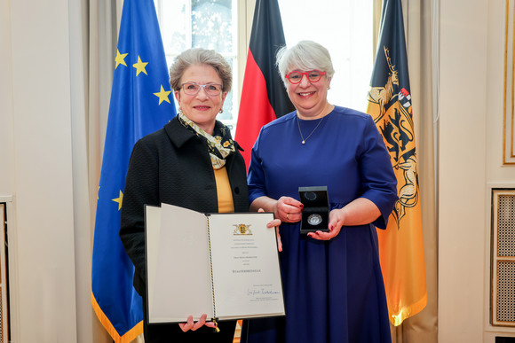 Auszeichnung Irene Armbruster mit Staufermedaille geehrt Staatsrätin Barbara Bosch (links) überreicht Irene Armbruster (rechts) die Staufermedaille und eine Urkunde. Im Hintergrdund stehen Fahnen.