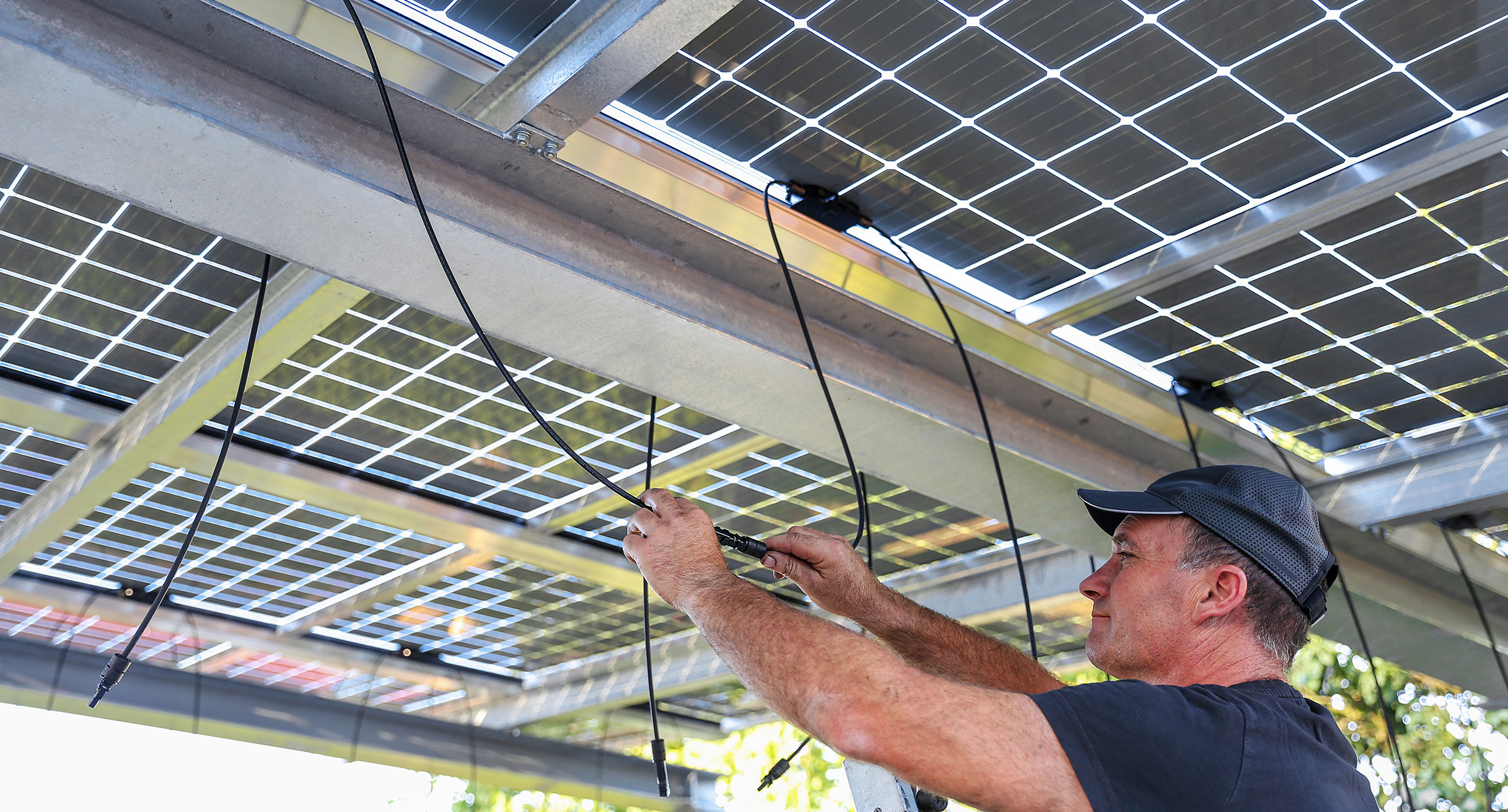 Ein Mann installiert Solarzellen auf dem Dach eines Carports.']