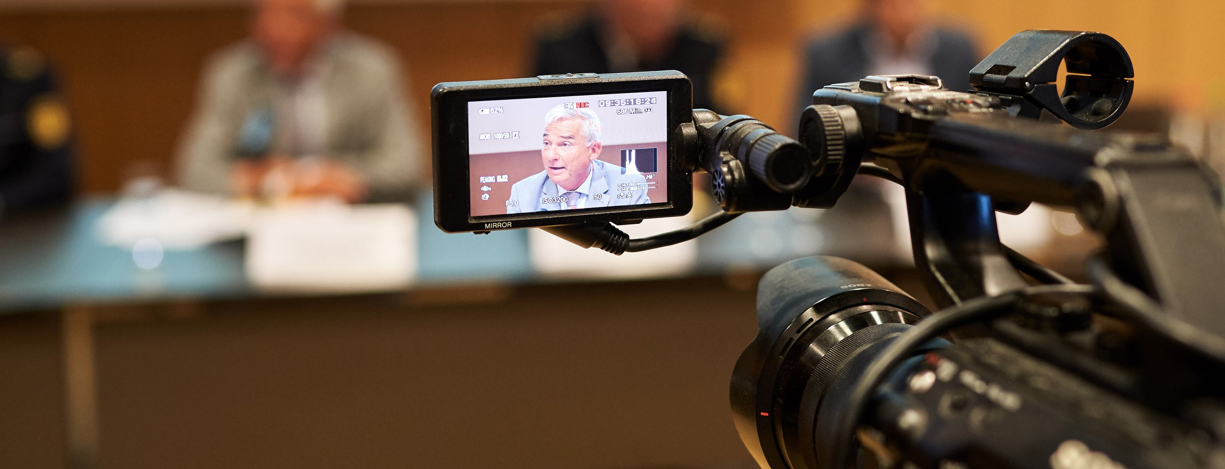 Blick durch eine Kamera auf Minister Thomas Strobl bei einer Pressekonferenz. Quelle Innenministerium, Fotograf Steffen Schmid. 
